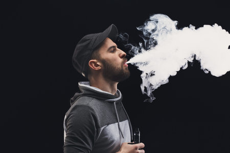 Young Man Exhales Vapor From an Electronic Cigarette in a Dark Setting During a Vaping Session