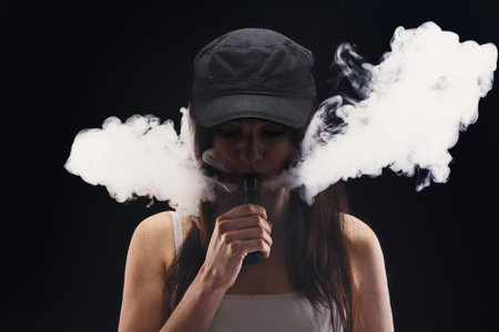 Woman in Hat Vaping Indoors With Smoke Around Her in a Dark Setting
