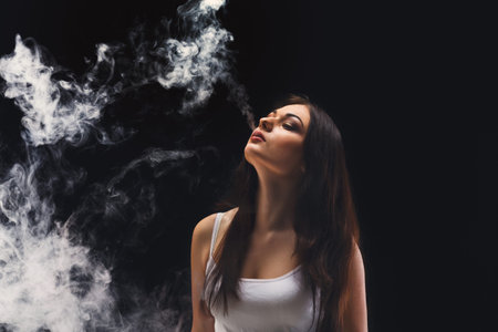 Woman Exhales Smoke in Dark Space During Indoor Activityの写真素材