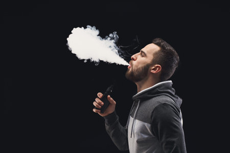 Man Exhales Vapor From Vape Device in Studio During Nighttime