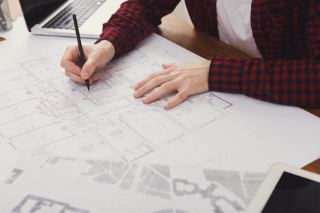 Person Working on Architectural Plans at Desk With Laptop and Drawings in Office