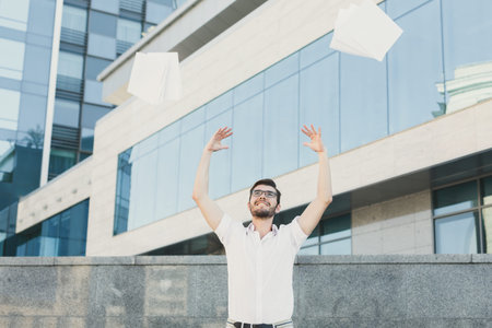 Man Throws Papers in the Air in Front of a Modern Building During the Day in the Cityの写真素材