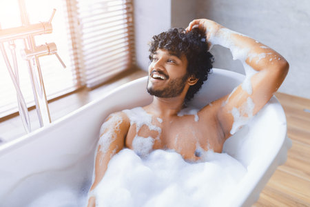 Young Man Enjoys Bath in Modern Tub With Bubbles and Sunlight Coming Through Window
