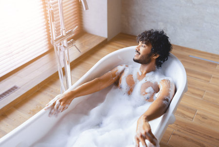 Man Relaxes in Bathtub With Bubbles and Sunlight in Modern Bathroom