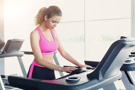 Woman Exercises on Treadmill in Gym During Daytime While Focusing on Workout Routine and Settings