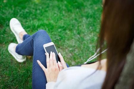 Young Person Uses a Smartphone While Sitting on Grass in a Park During the Day