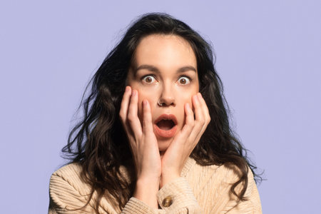Woman Shows Surprise With Hands on Face in Front of Solid Background During Daytime