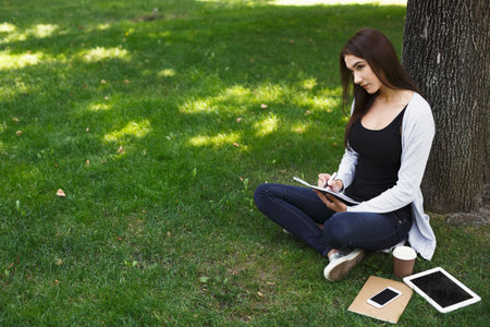 Creating Notes in the Park While Enjoying a Sunny Afternoon With a Coffee Cup and Devices Around