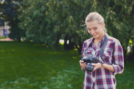 Young Woman Enjoys Photography While Standing in a Green Park Space Surrounded by Trees and Natureの写真素材