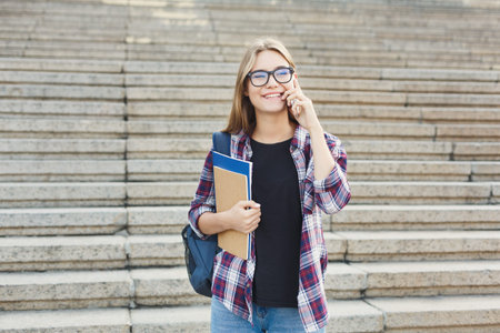 Young Woman With Glasses Talks on Phone While Holding a Folder Near Stone Stairs