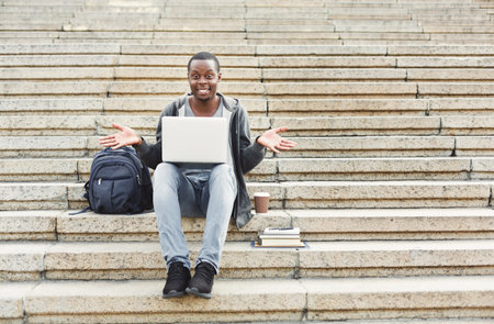 Young Man Using Laptop on Steps With Backpack and Coffee Cup During Daytime