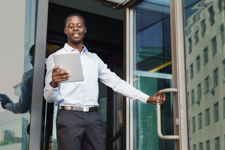 Business Man Steps out of Office While Looking at Tablet in Hand at a City Location