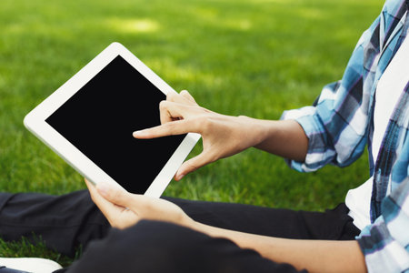 Person Sitting on Grass Using Tablet in Sunny Outdoor Setting
