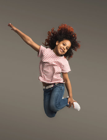 Happy little black girl jumping at studio background