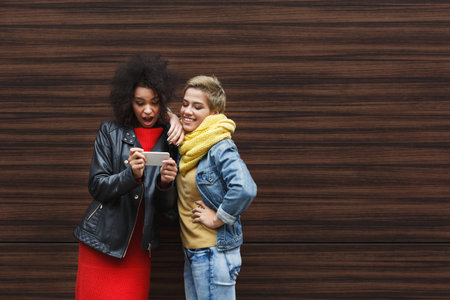 Two Friends Share a Moment While Looking at a Phone in a Cozy Indoor Settingの写真素材