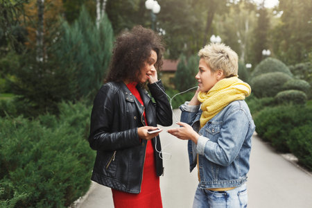 Two Friends Share Music While Walking in a Park During Autumn Season