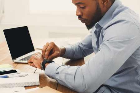 Man Checks Smartwatch While Sitting at Desk During Work Hours in Modern Office Setting