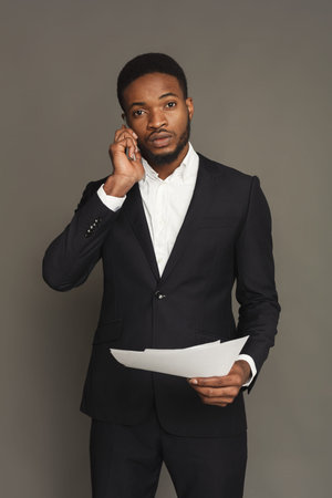 Business Man in Suit Talking on Phone and Holding Papers in Studio Settingの写真素材
