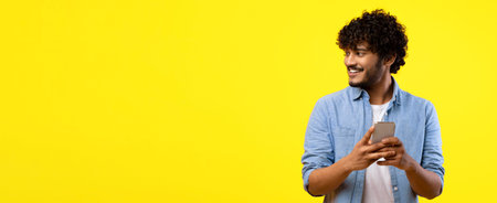 Young Man Holding Smartphone While Smiling in Front of a Bright Yellow Background