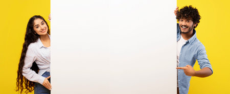 Young Adults Hold Blank Sign and Smile Against Bright Yellow Backgroundの写真素材