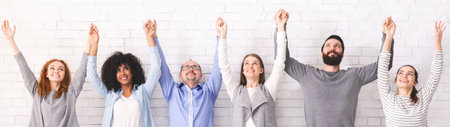Group of happy diverce people holding hands, raising arms up, panorama