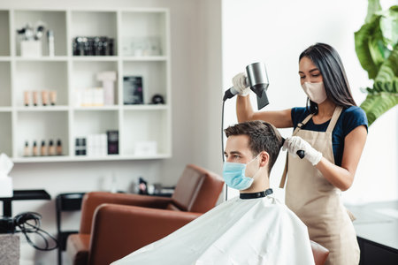 Hairdresser and male client in protective mask at barber shop, empty space