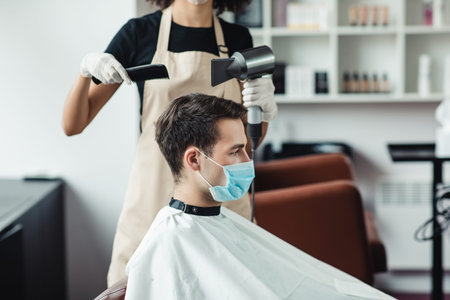 Young man in protective mask getting haircut at barbershop