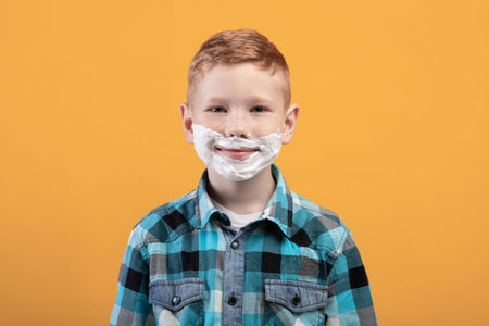 Playful little boy shaving face over yellow background
