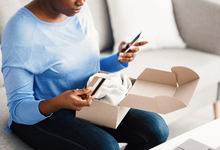 Black lady sitting with box, credit card and smartphone