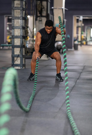 Muscular black guy having work out with ropes at gym