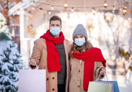Couple in face masks holding shopping bags on winter day