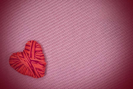 Red heart made of thread on a pink knitted pattern background with an empty space is a design material for Valentines, holiday cards, backgrounds.の写真素材