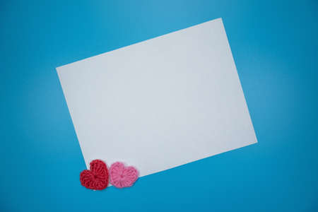 White paper with knitted decorative hearts on a blue background design template.の写真素材