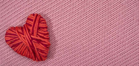 Red heart made of thread on a knitted pink textile texture background.の写真素材