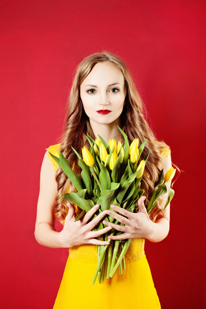 Young Beautiful Blonde Woman with Yellow Tulip Flowers on Bright Colorful Backgroundの写真素材