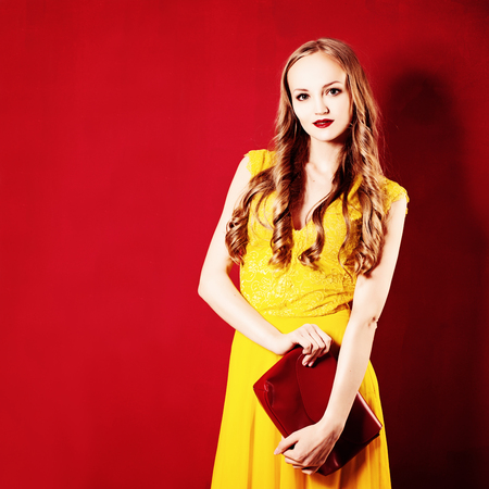 Fashion Woman with Curly Blond Hair. Girl wearing Yellow Dress on Bright Red Backgroundの写真素材