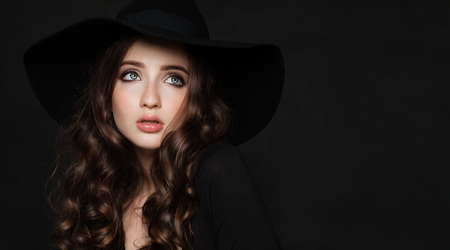 Beautiful Brunette Woman with Perfect Curly Hairstyle and Makeup. Perfect Model wearing Black Hatの写真素材