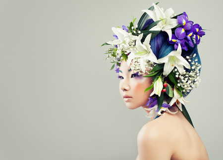 Beautiful Asian Model Woman with Colorful Flowers and Fashion Makeup. Spring Fashion Girl with White Lily and Iris Flowersの写真素材