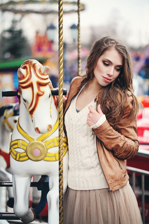 Young woman fashion model with long wavy brown hair and makeup on merry-go-round outdoorsの写真素材
