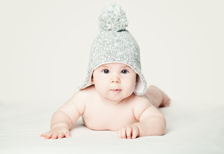 Baby in knitted hat lying on white blankett, portrait. Pretty little child (3 months old)の写真素材