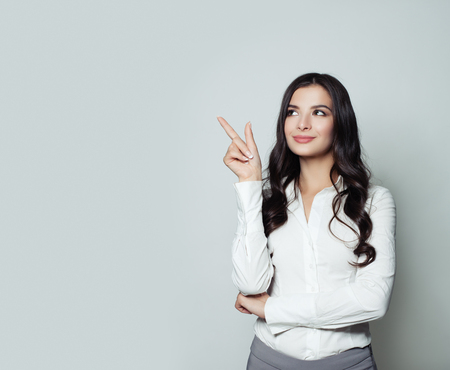 Business woman pointing her finger up on gray background with copy space. Friendly woman portrait, advertising marketing and product placement conceptの写真素材