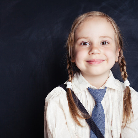 Portrait of cute little girl. Happy child smiling on empty blackboard background with copy space. Back to school.の写真素材
