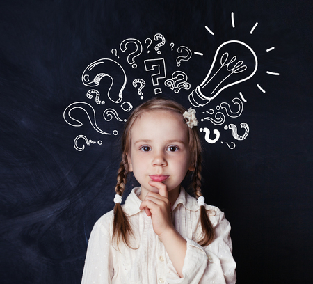 Smart child schoolgirl with lightbulb and chalk question marks on school blackboard background. Idea conceptの写真素材