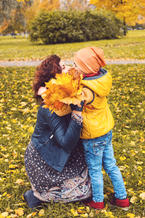 Mother and son with fall leaves having fun in autumn park outdoors. Happy expressions. Love care and positive relations. Mum and son together.の写真素材