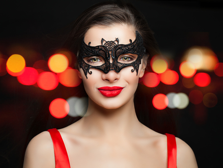 Young smiling woman in sexy carnival mask on abstract red night glitter bokeh backgroundの写真素材