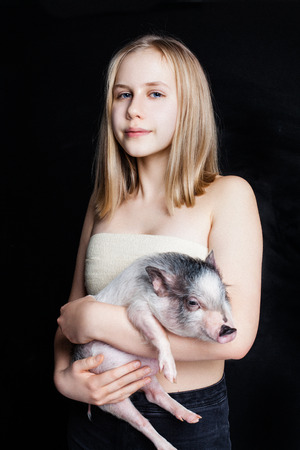 Cute teenager girl holding pig on black background, portraitの写真素材