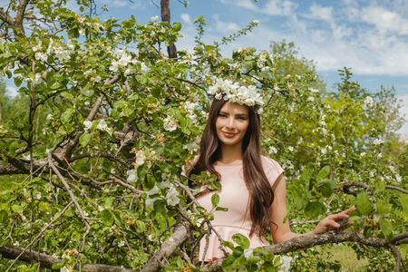 Smiling woman in spring flowers garden outdoors. Beautiful fashion model girl on blue sky, green leaves and apple tree flowers background outdoorの写真素材