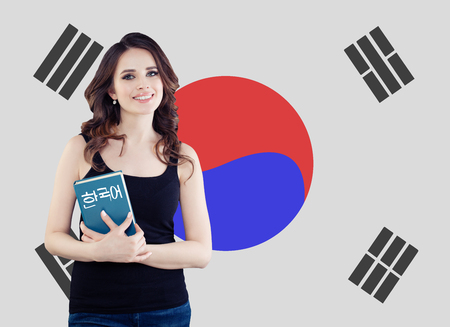 Learn korean language. Pretty young woman student with book against the South Korea flag backgroundの写真素材