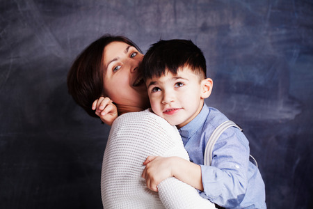 Happy mother and son having fun, laughing and hugging. Beautiful woman and her cute little child boy playing and smiling on chalkboard backgroundの写真素材