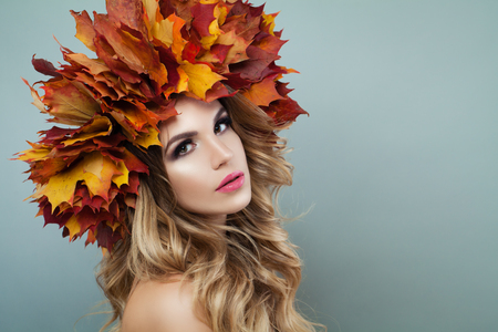 Woman face closeup. Autumn model woman with makeup, blonde hair and fall leavesの写真素材